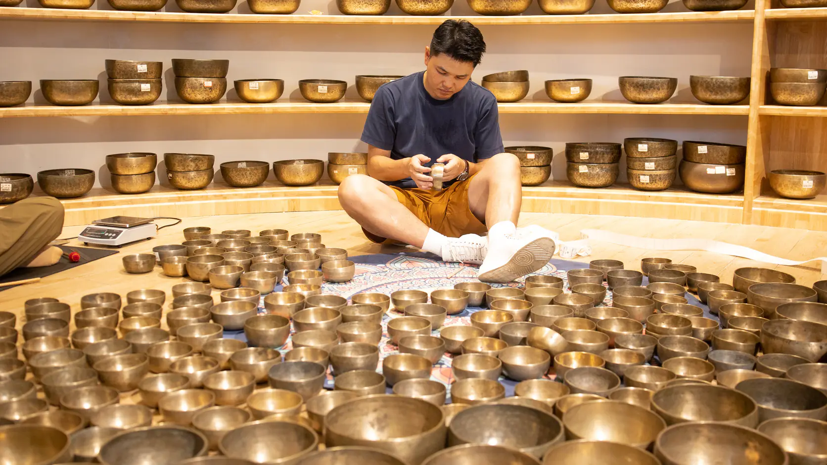选钵人员坐在多层颂钵陈列前，地面铺开多只候选器物进行逐只检查