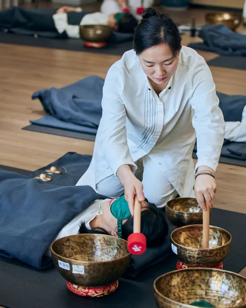 A facilitator works through several singing bowls among participants while maintaining spacing between instruments and individual places