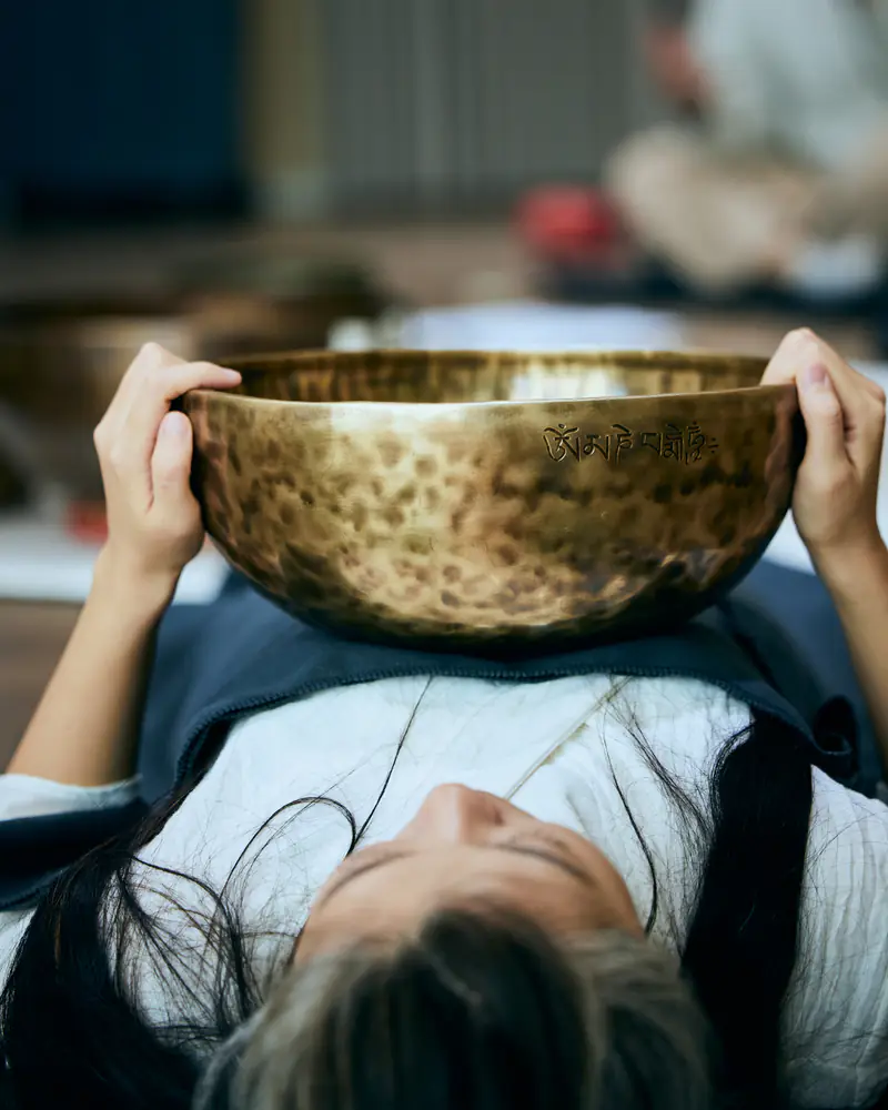 A learner steadily holds a metal singing bowl with both hands during guided practice