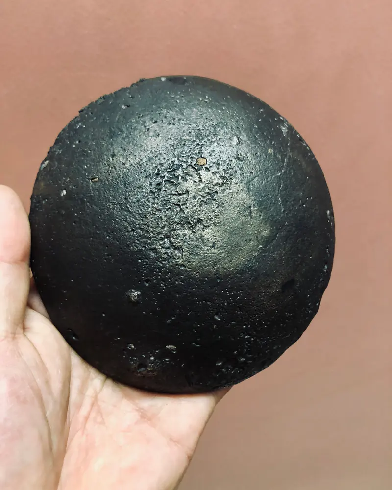 手中托着一只深色铜钵，近距离展示锤纹与器底表面