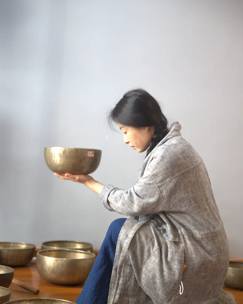 真人托持一只旧钵，在多只颂钵之间观察器形与操作手感